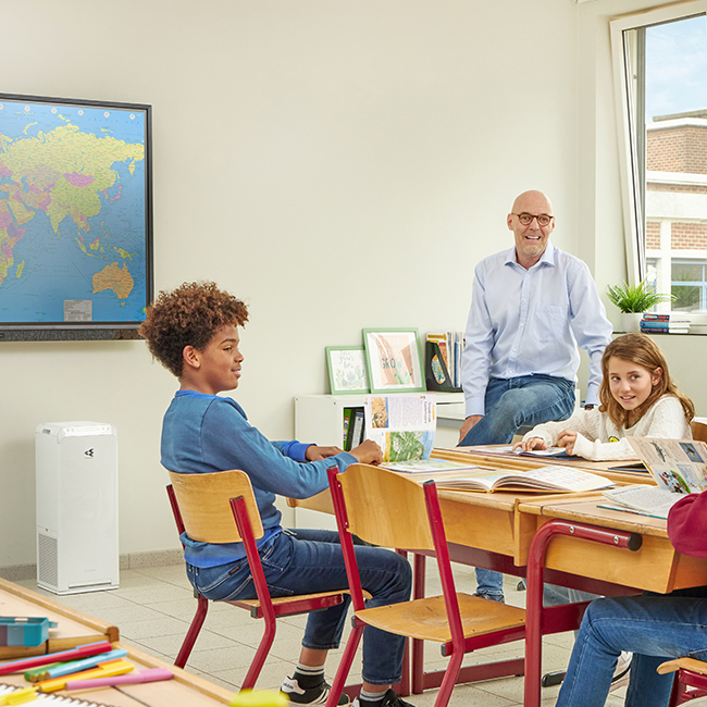 Toont de Daikin MCK55W luchtreiniger in een klasruimte