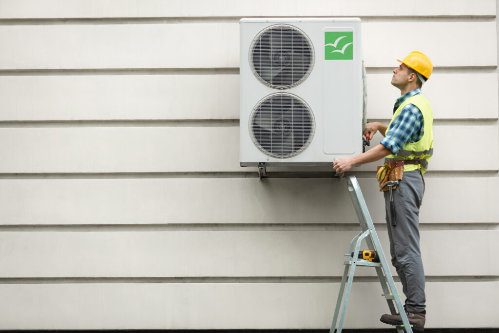 Toont een man op een ladder naast een airco buitentoestel
