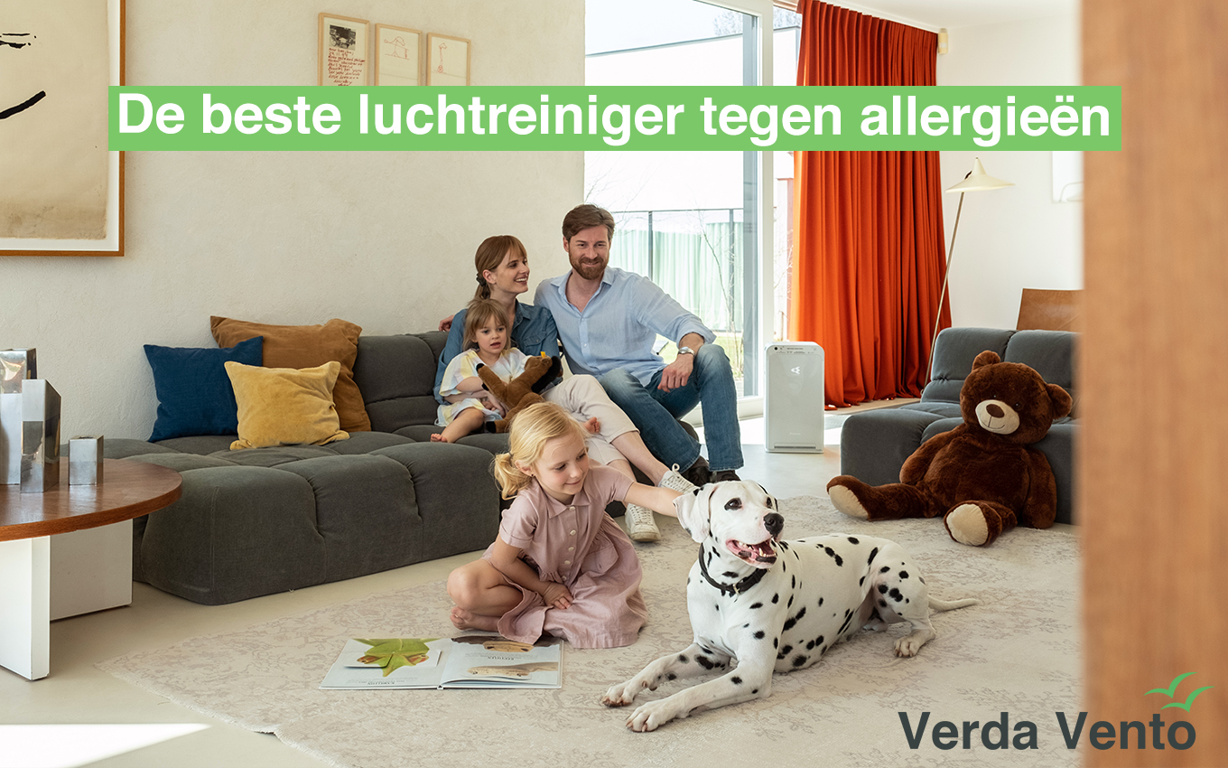 Toont een familie in hun living. De vader en moeder zitten in de zetel terwijl de dochter en hond op de grond zitten. In de hoek staat er een luchtreiniger